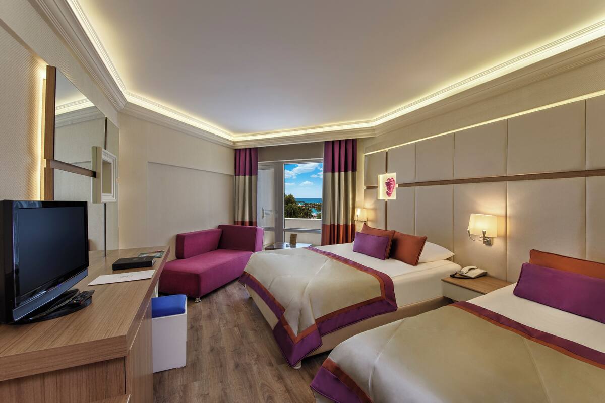 A hotel room with two beds, a TV, a desk, and a view of the outdoors.