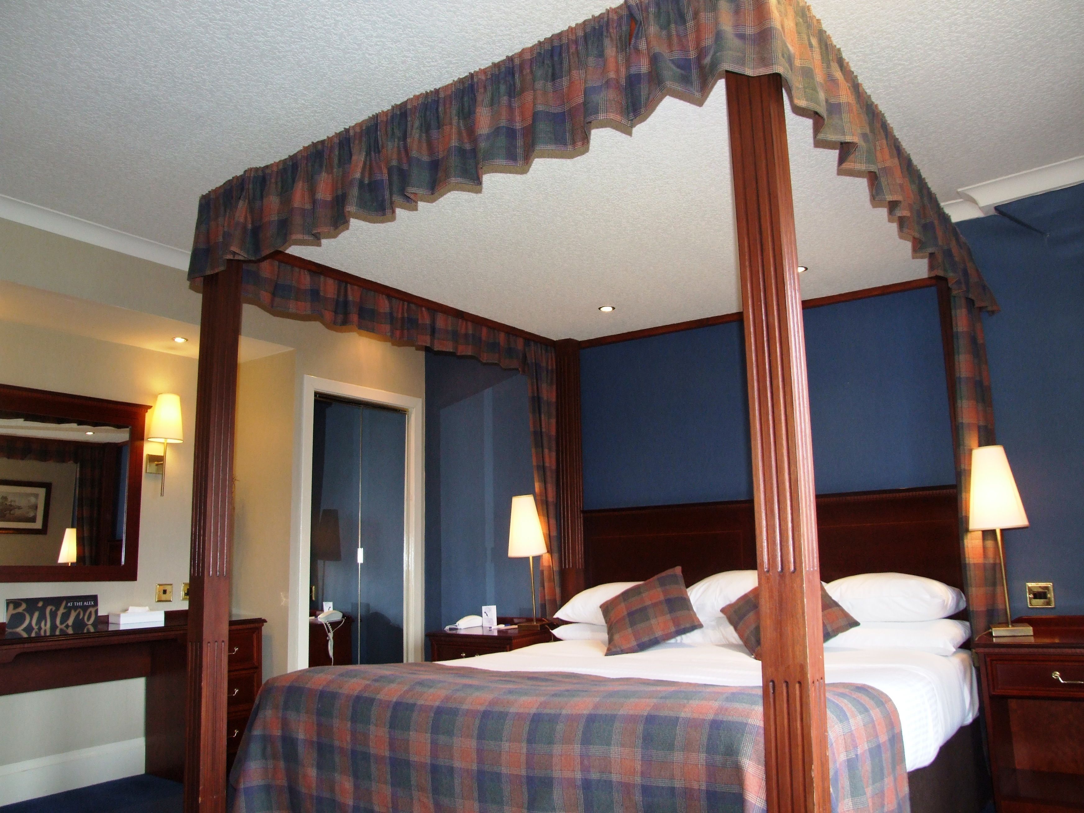 A four-poster bed with a plaid bedspread, a wooden headboard, and two bedside lamps.