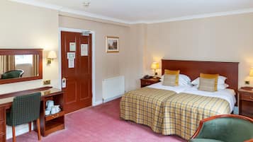 A hotel room with a bed, a desk, a chair, a radiator, and a door.