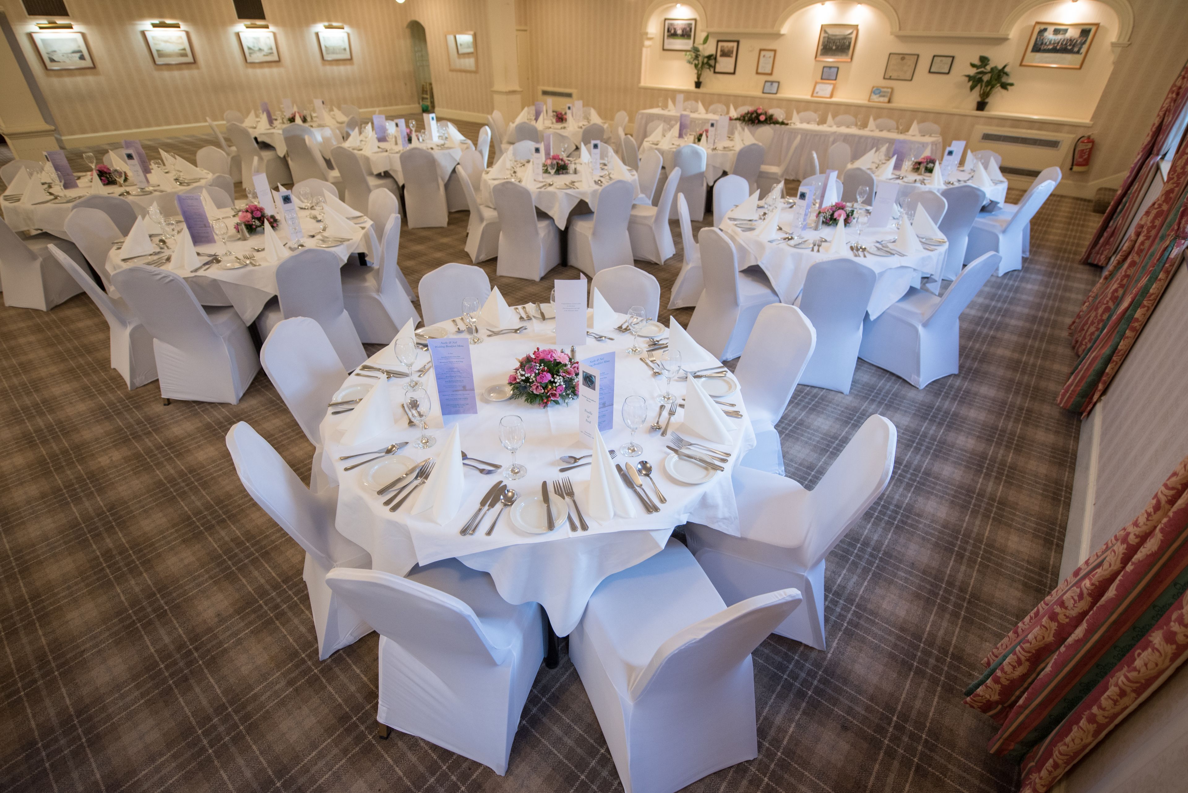 A banquet hall with round tables set for dining, white chairs, and floral centerpieces.