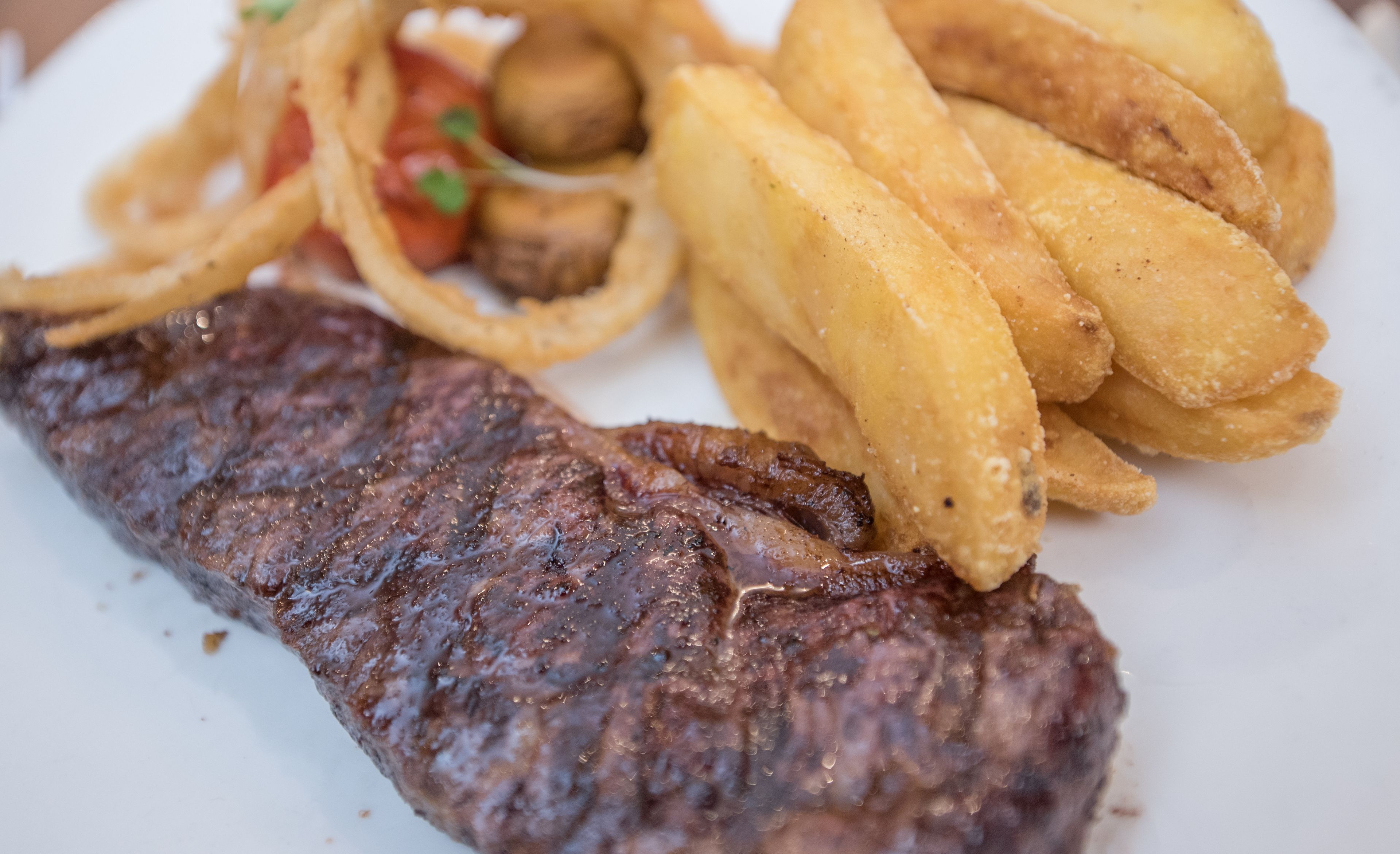 A plate with a grilled steak, French fries, and onion rings.