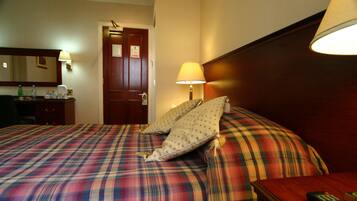Een hotelkamer met een ruitdessin sprei, een houten hoofdbord, een nachtkastje met lamp en een deur met een bordje.