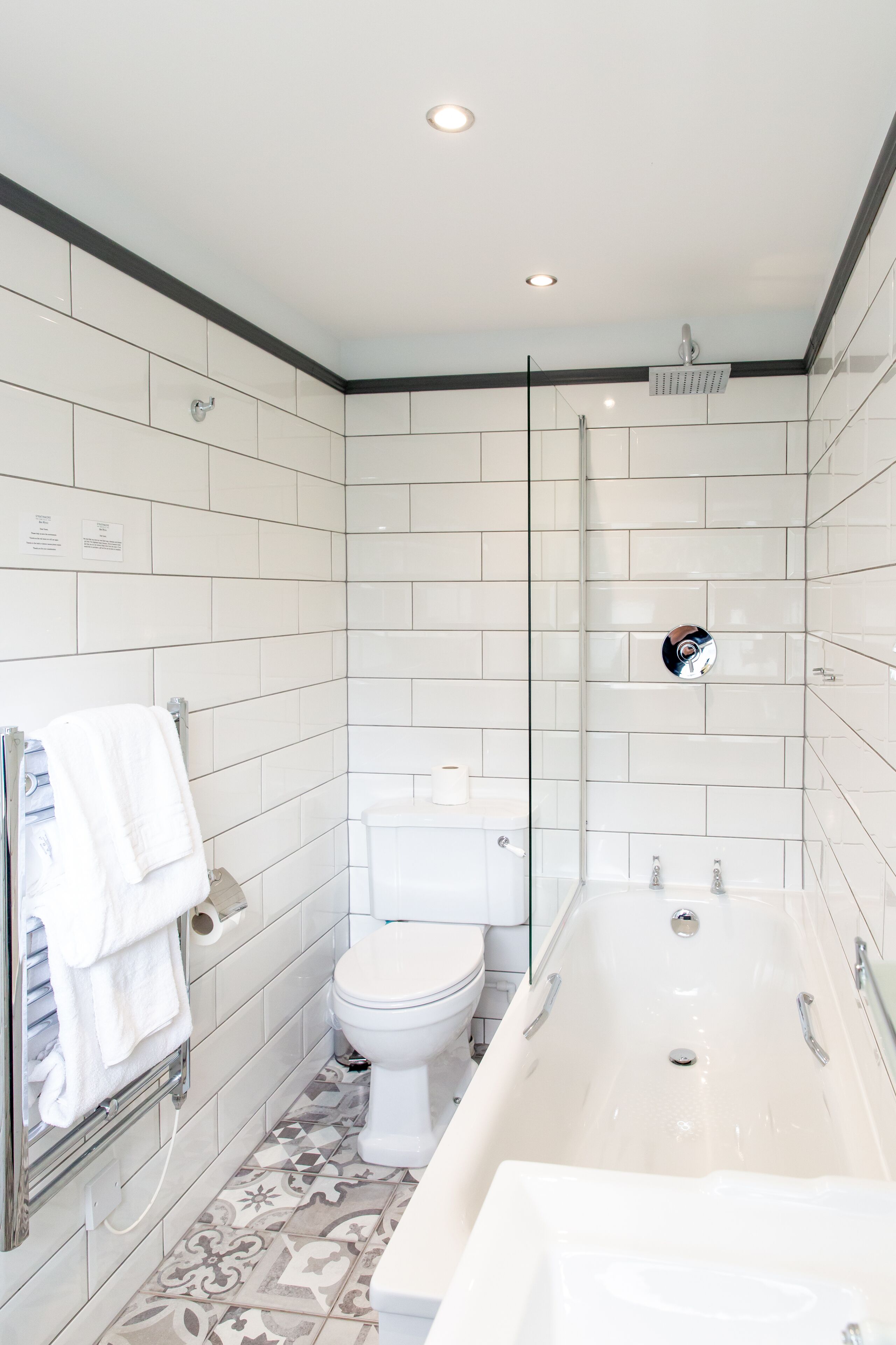 A modern bathroom with white tiles, a toilet, a bathtub, and a shower.