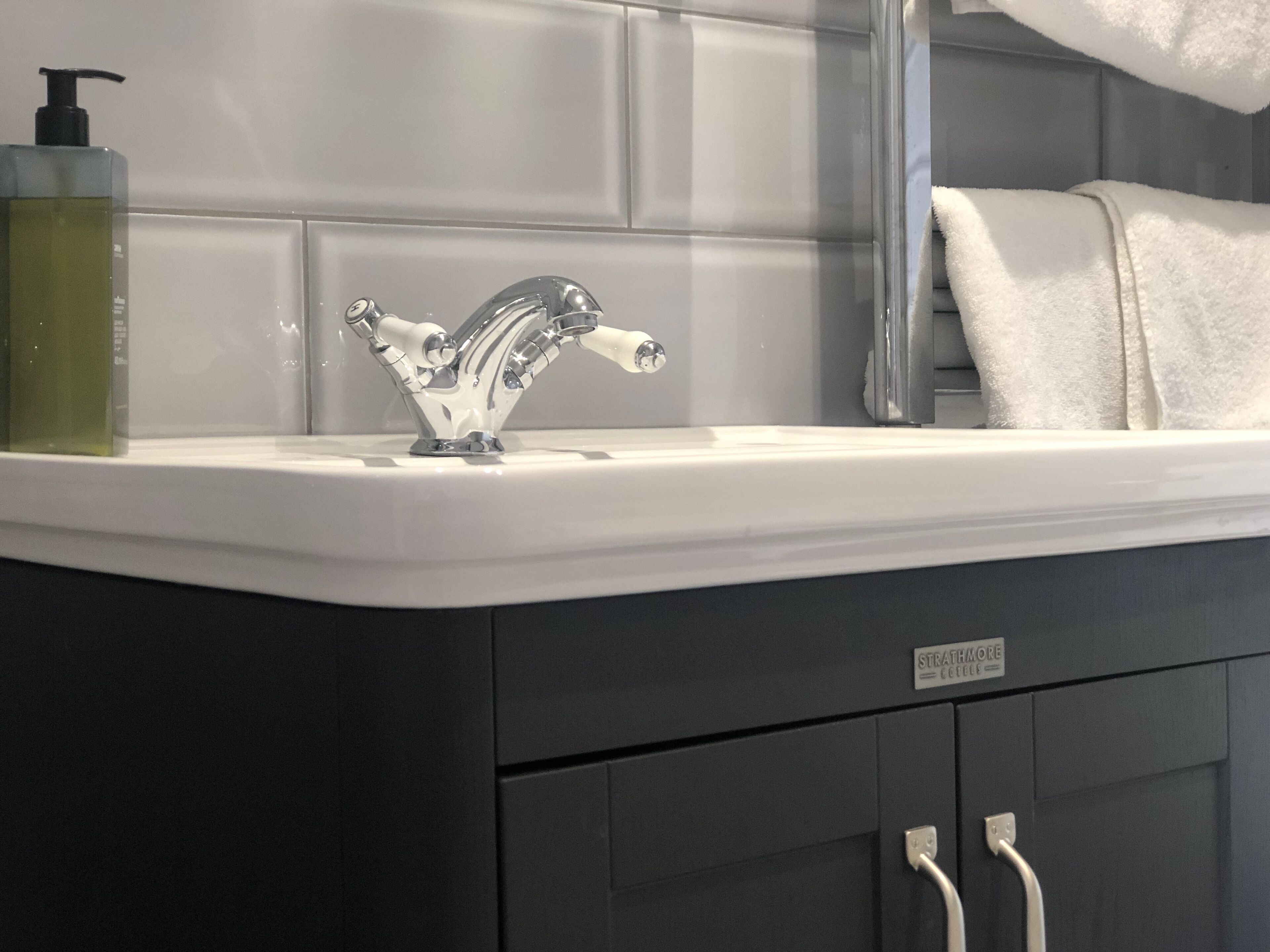 Un baño con un lavamanos moderno, un dispensador de jabón y un perchero para toallas.