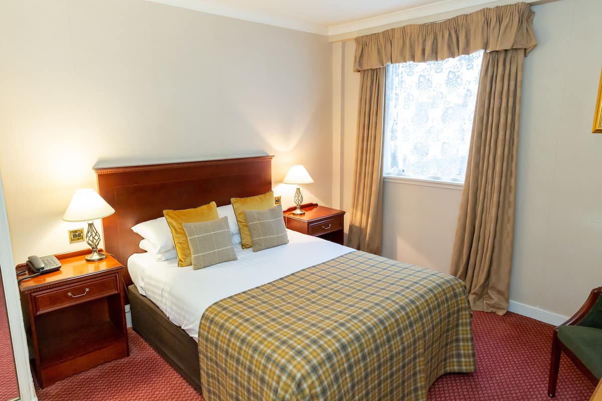 A hotel room with a large bed, two bedside tables, a nightstand, a lamp, a telephone, and a window with curtains.