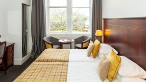 Une chambre d’hôtel avec deux lits, une petite table, deux chaises, une lampe et une vue sur les arbres par la fenêtre.