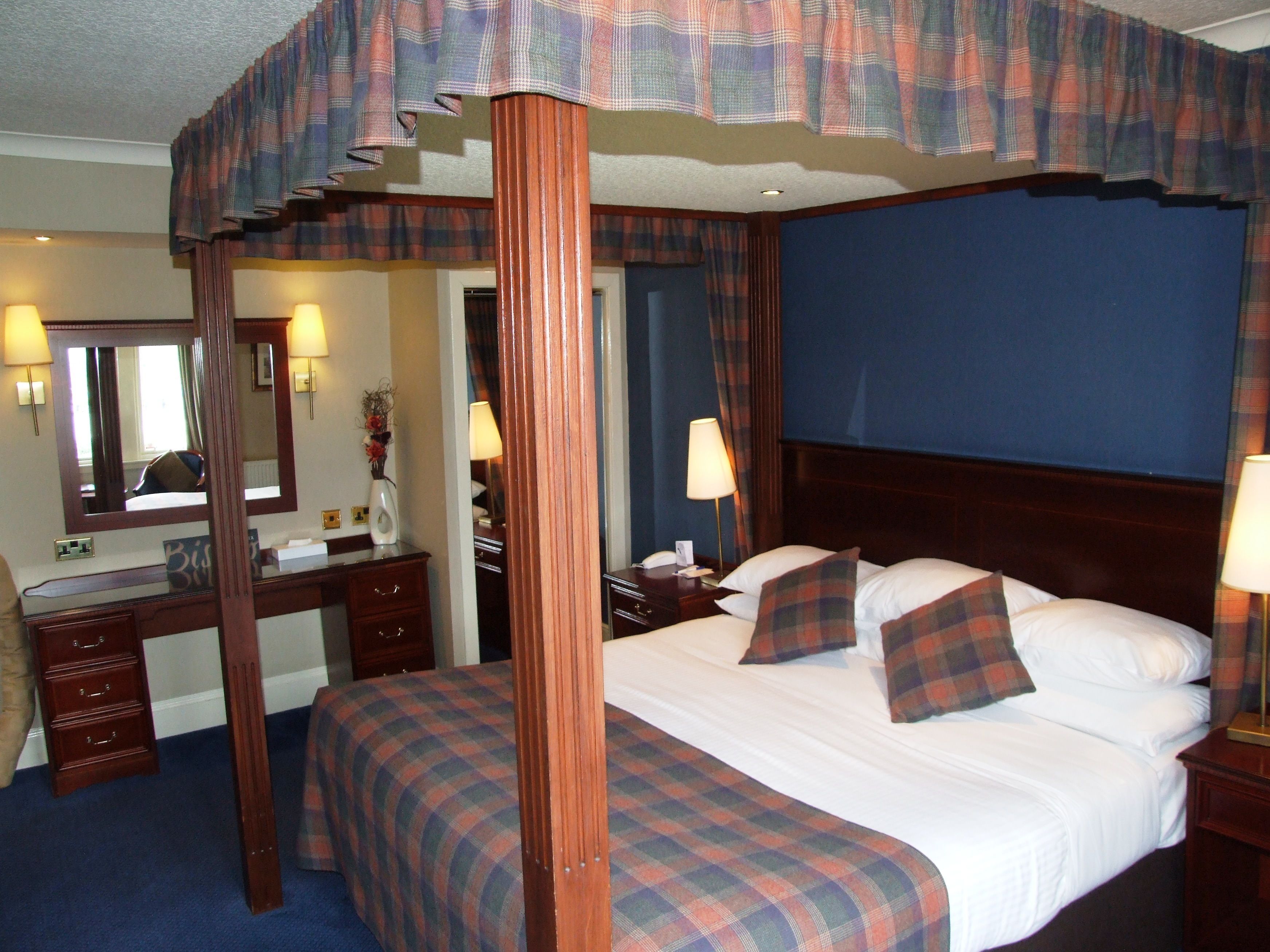 A hotel room with a four-poster bed, a desk with a mirror, and a dresser.