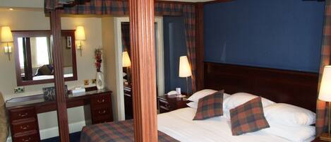 A hotel room with a four-poster bed, a desk with a mirror, and a dresser.