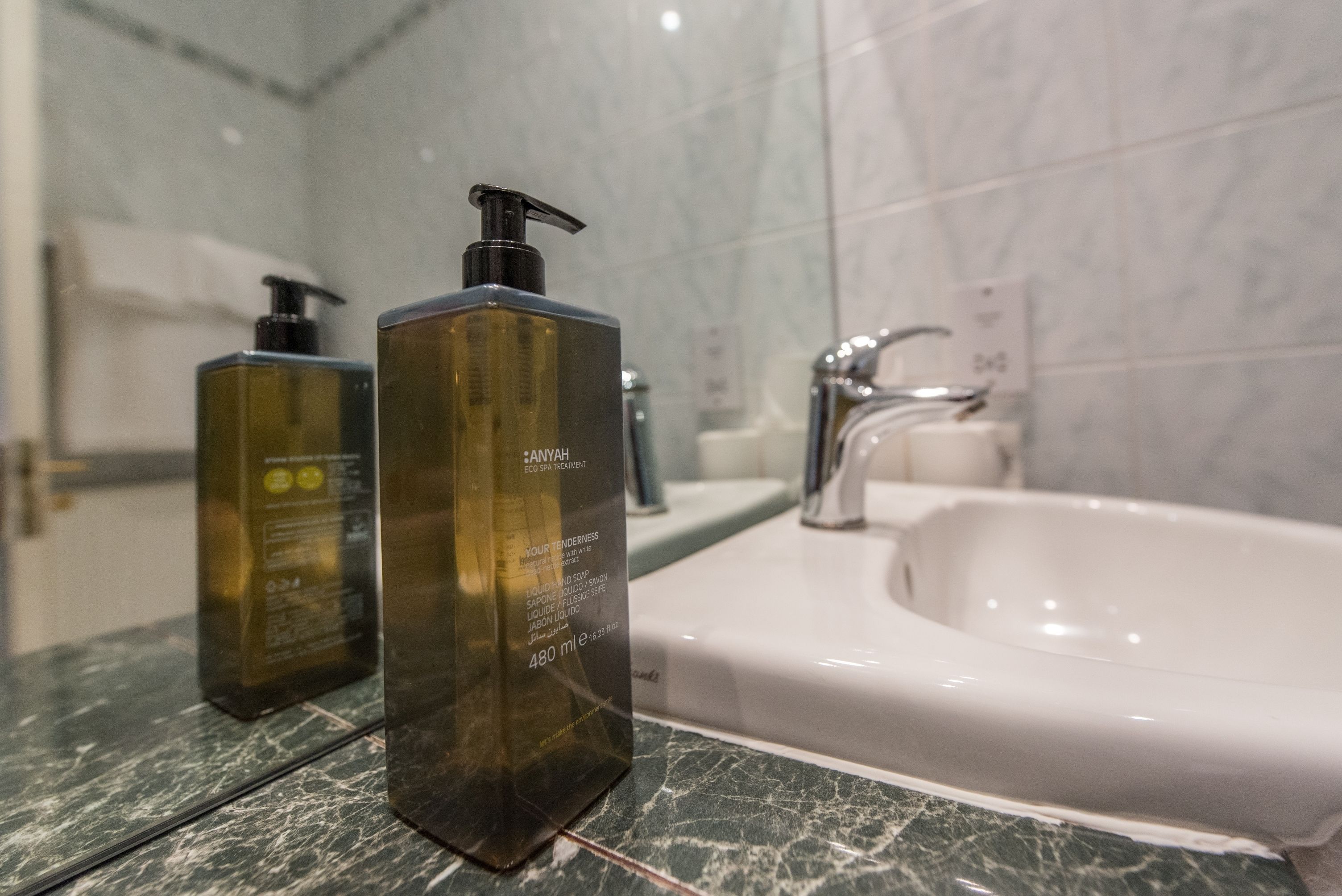 Un bagno con piano in marmo, lavandino bianco e due flaconi di Anyah Eco Spa Treatment sul ripiano.