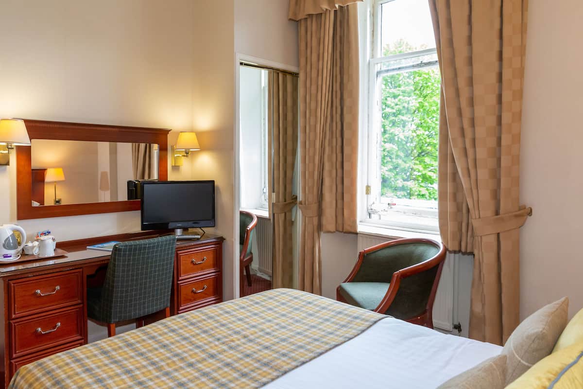 A hotel room with a bed, desk, chair, television, and a window with curtains.