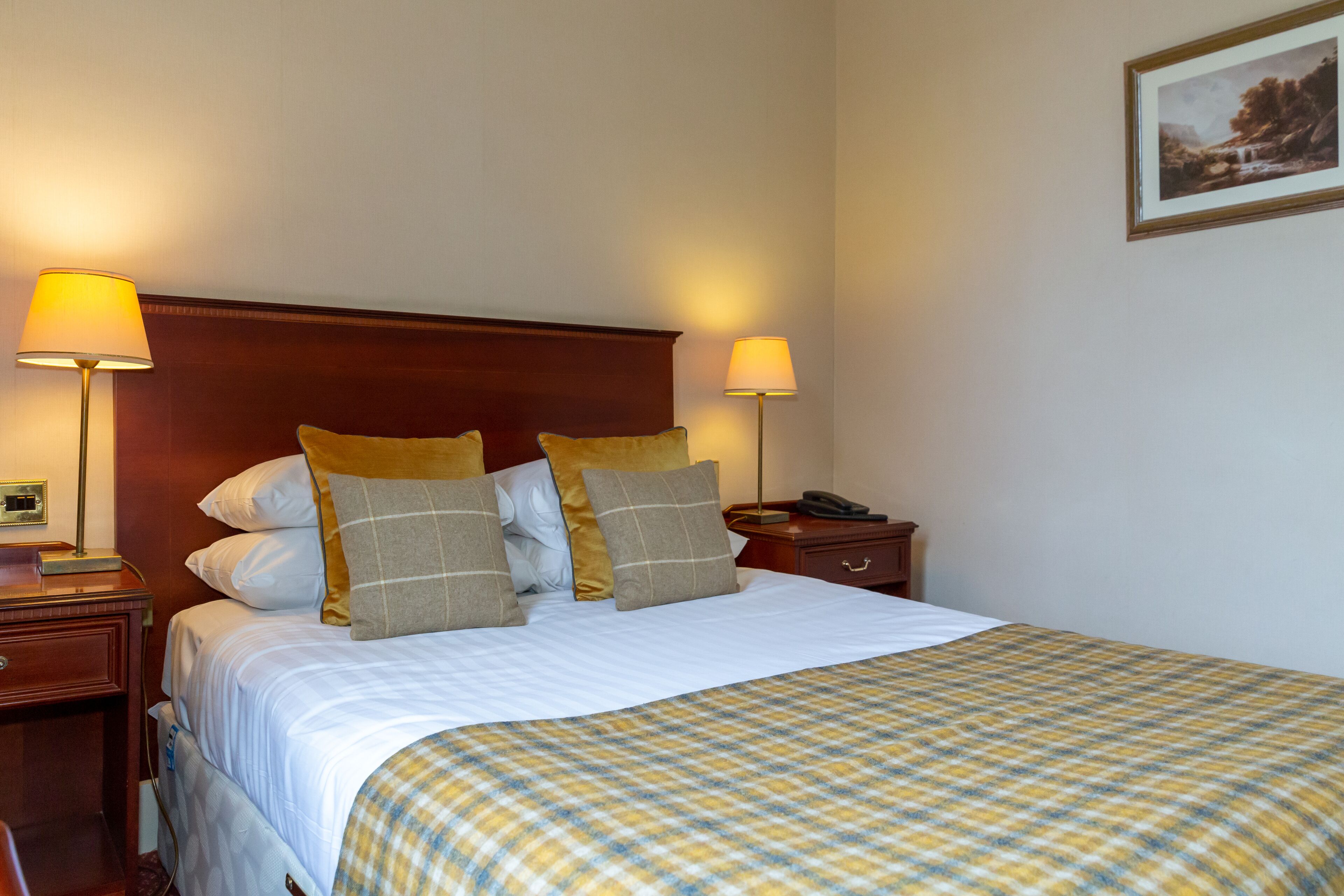 A neatly made bed with a checkered bedspread, two bedside lamps, and a nightstand with a telephone.