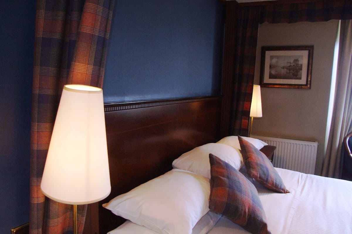A hotel room with a large bed, plaid curtains, and two bedside lamps.