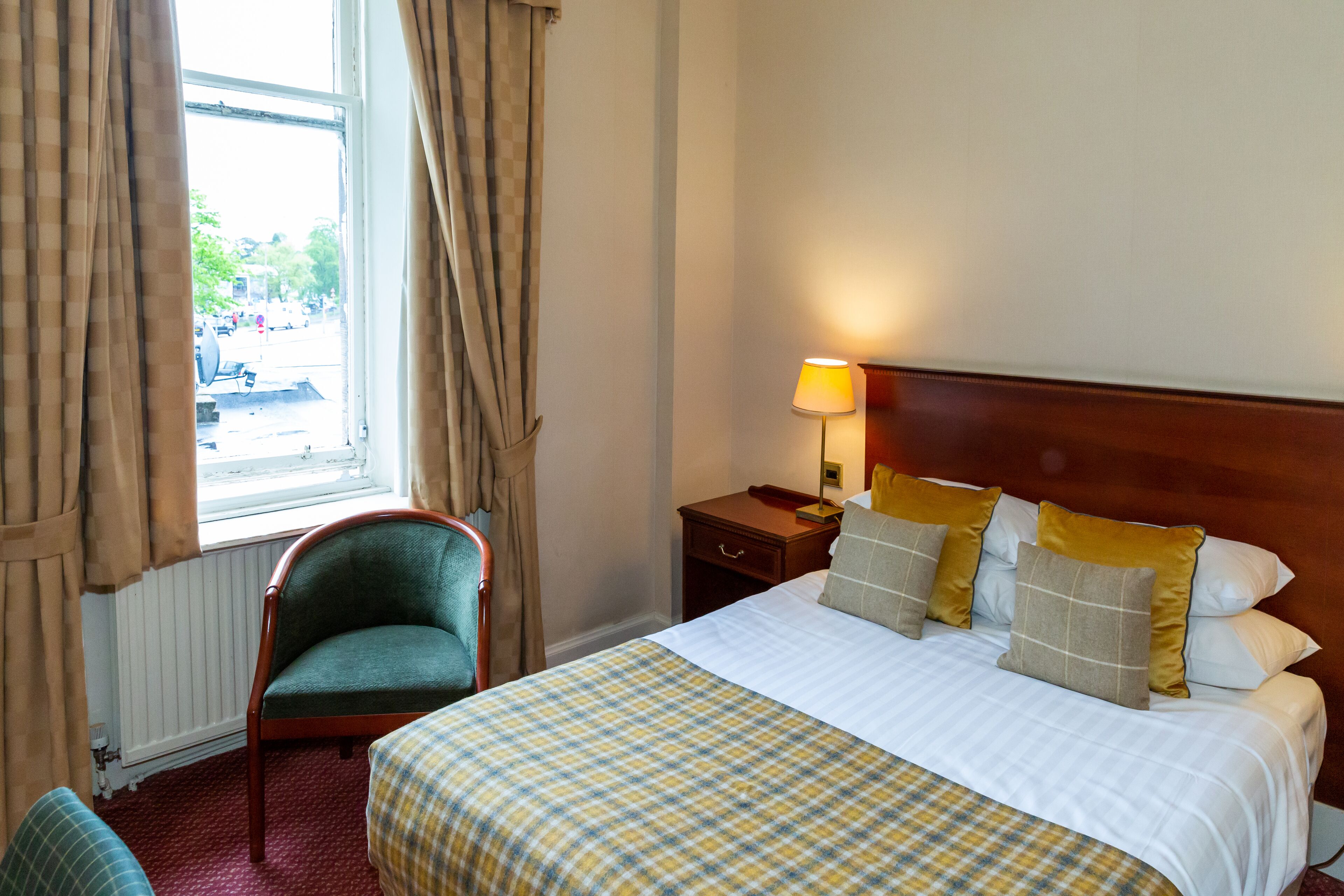 Ein Hotelzimmer mit Bett, Sessel, Nachttisch und einem Fenster mit Vorhängen.
