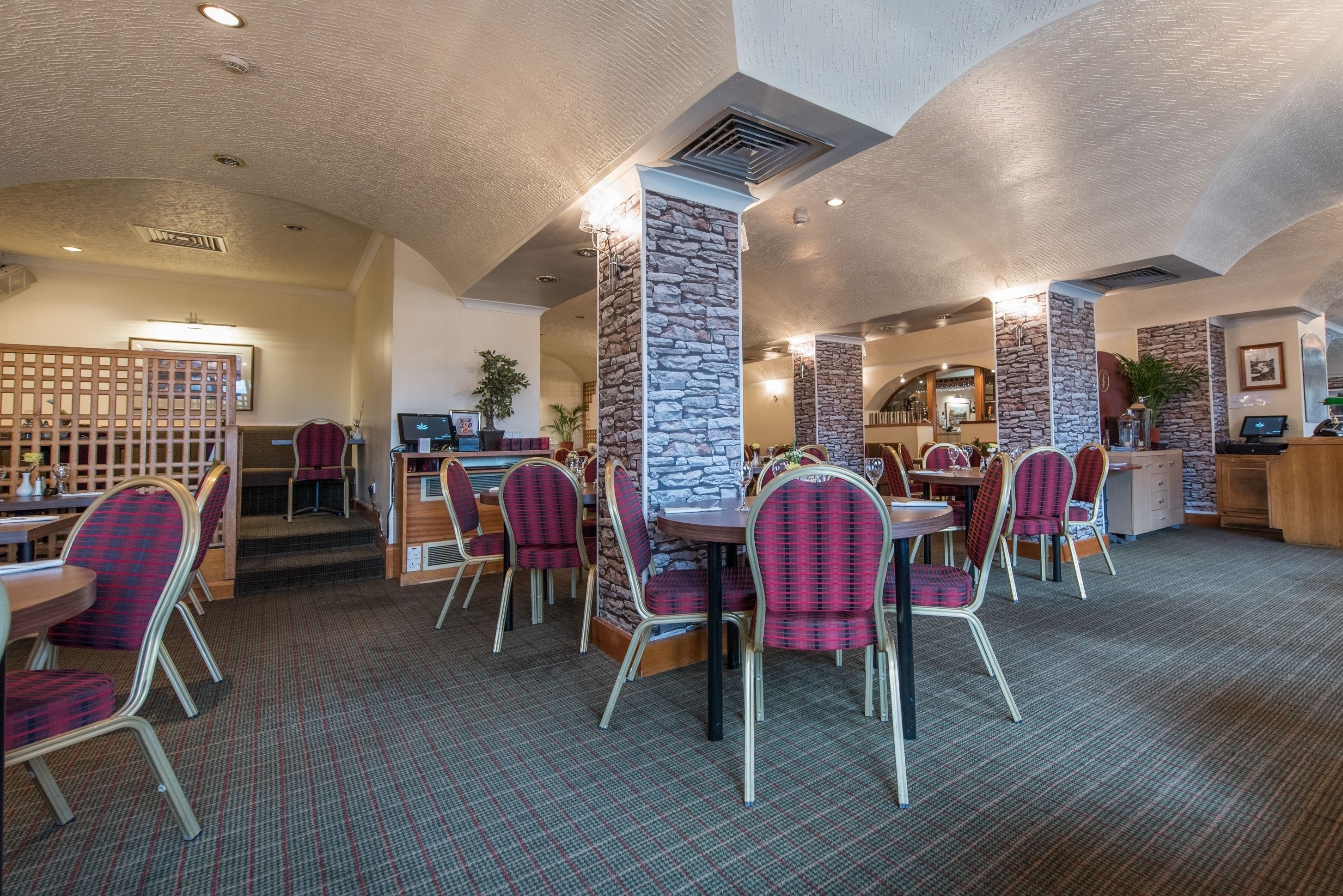 Un restaurant avec un plafond haut, des piliers en pierre et des chaises à carreaux rouges et noirs.