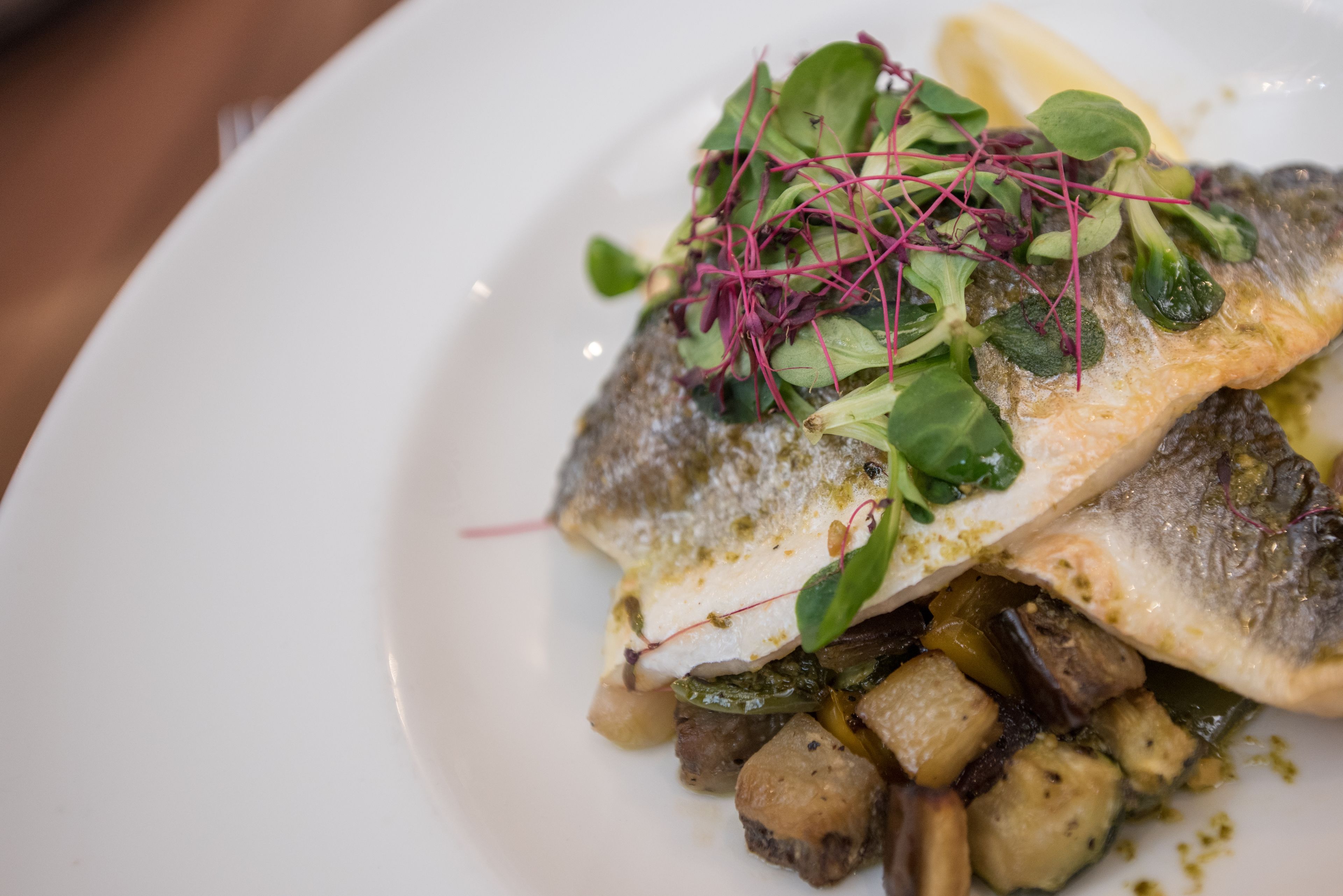 A plate with a fish, greens, and potatoes.