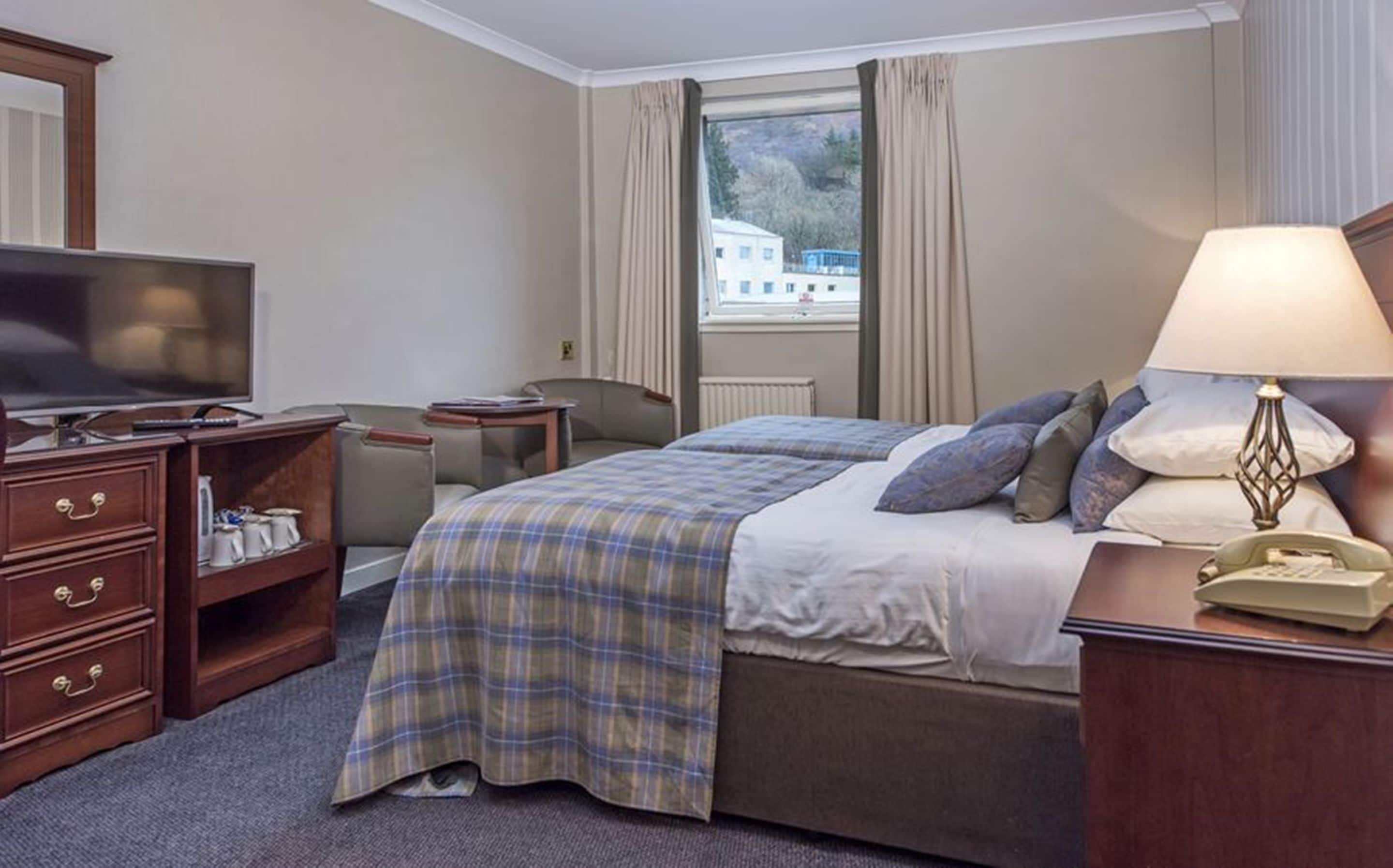 A hotel room with a bed, a television, a desk, and a lamp.