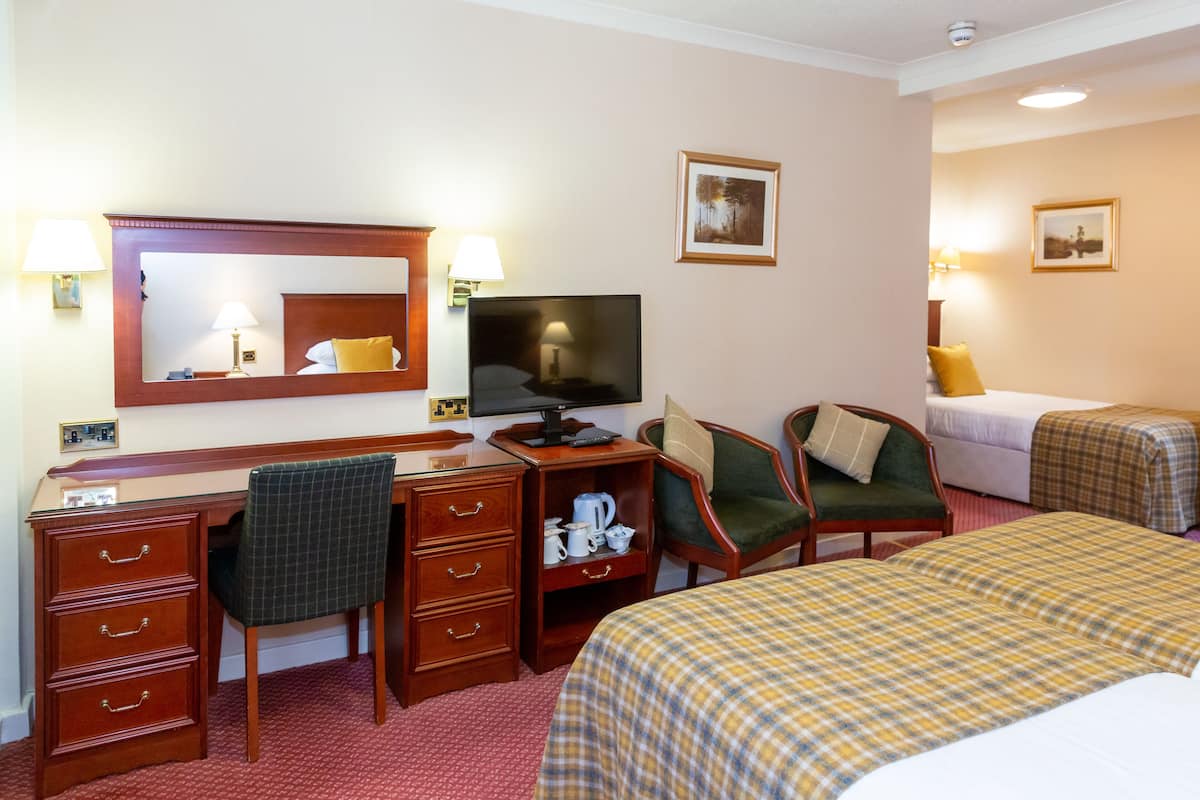 A hotel room with a desk, chair, television, two beds, and a small seating area.