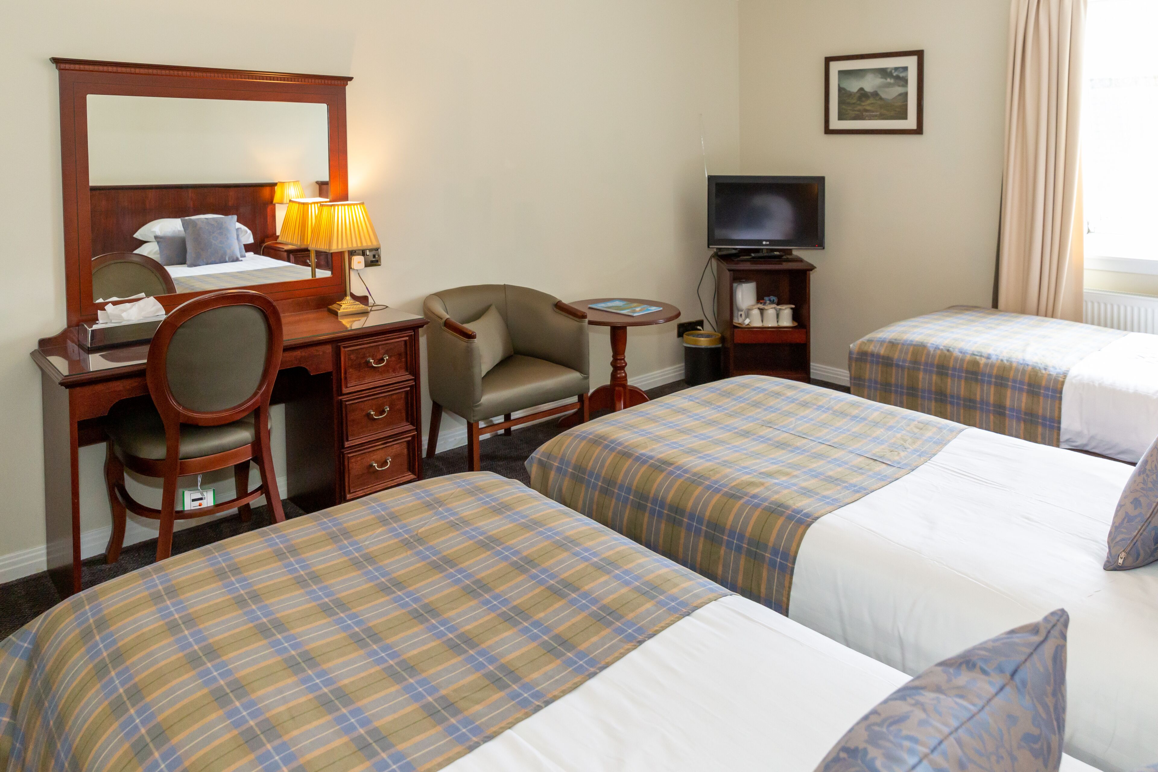 A hotel room with two beds, a desk with a chair, a television, and a small table.
