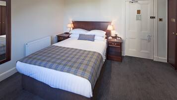 A hotel room with a large bed, two bedside tables with lamps, a wooden headboard, a white door, and a carpeted floor.