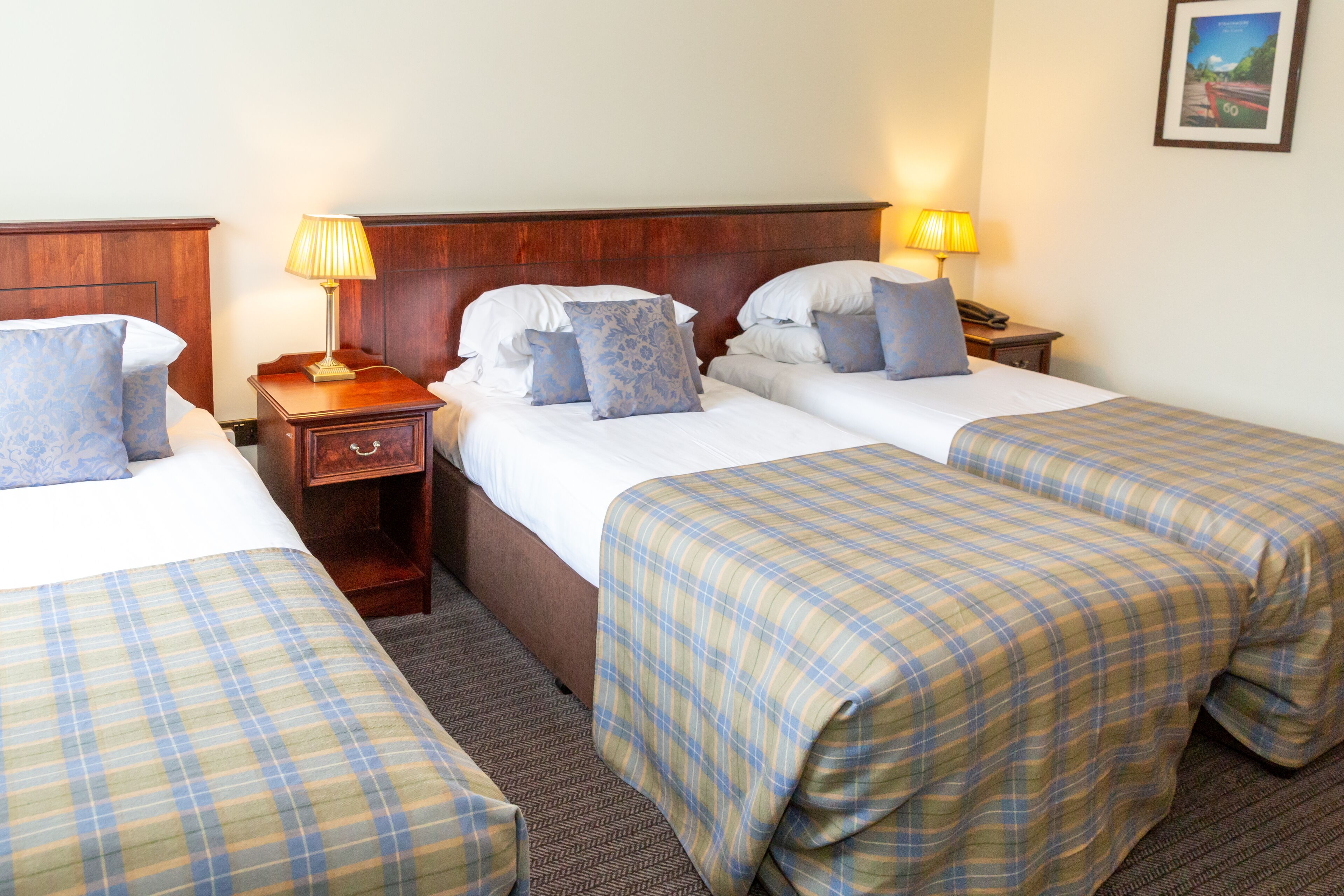 Ein Hotelzimmer mit zwei Einzelbetten, jeweils mit einem hölzernen Kopfteil, einem Nachttisch mit Lampe und einer kleinen Schublade.