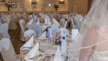 A banquet hall with round tables set for a wedding reception, featuring white tablecloths, chairs, and a bride in a white wedding dress.