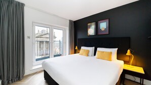 Habitación de hotel con una cama grande, dos mesitas de noche, una ventana con cortinas y una obra de arte en la pared.