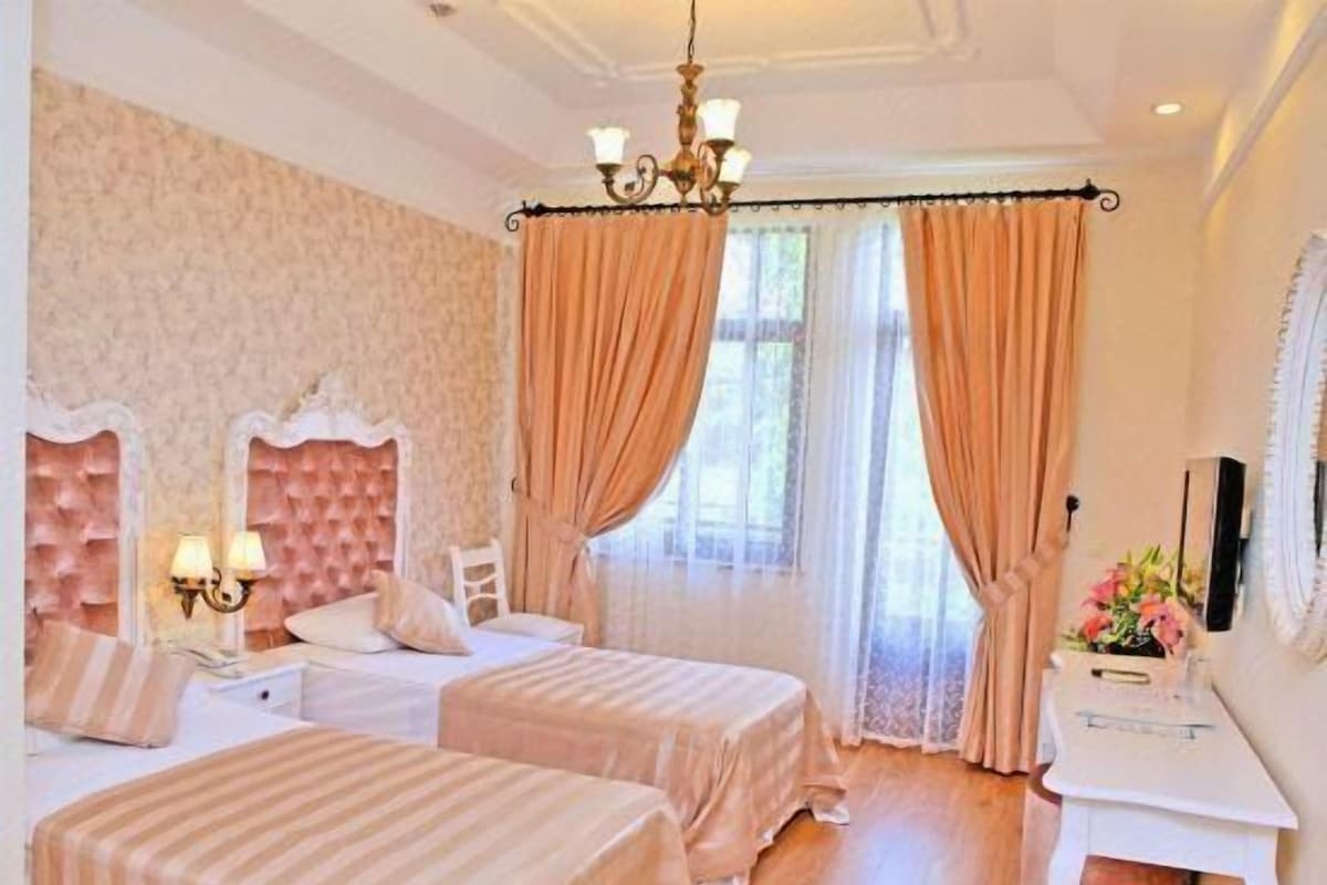 A hotel room with two beds, a desk, and a chandelier.