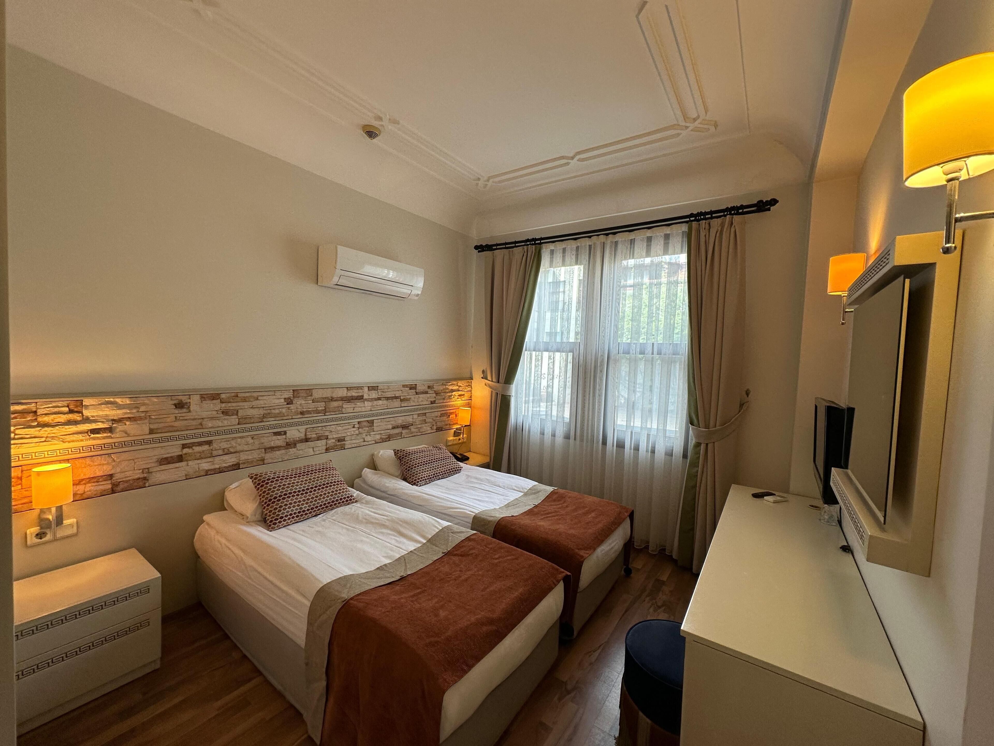Habitación de hotel con dos camas, un escritorio, un televisor y una ventana con cortinas.