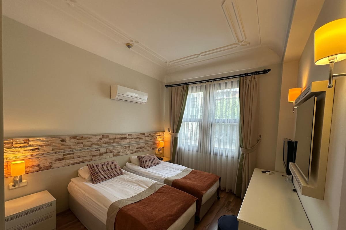 Habitación de hotel con dos camas, un escritorio, un televisor y una ventana con cortinas.