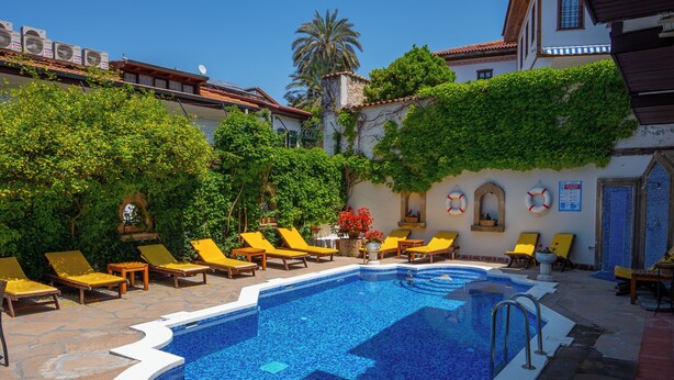 A swimming pool with tiled edges, surrounded by yellow lounge chairs and a stone patio. - Aspen Hotel - Special Class (Antalya)