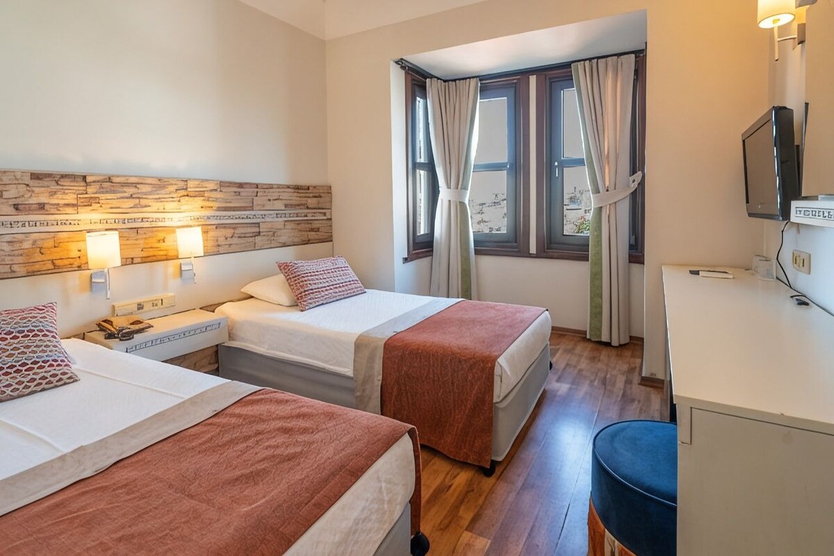 A hotel room with two beds, a desk, a television, and a window with curtains.