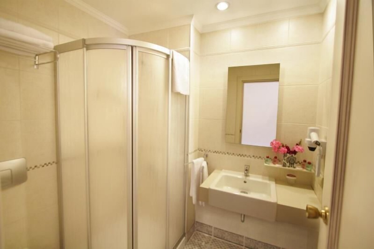 Een badkamer met een douchecabine van glas, een wastafel met spiegel en een klein plankje met toiletartikelen.