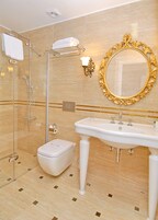Ein Badezimmer mit einer Duschkabine, einem Standwaschbecken und einem großen, verzierten Spiegel.