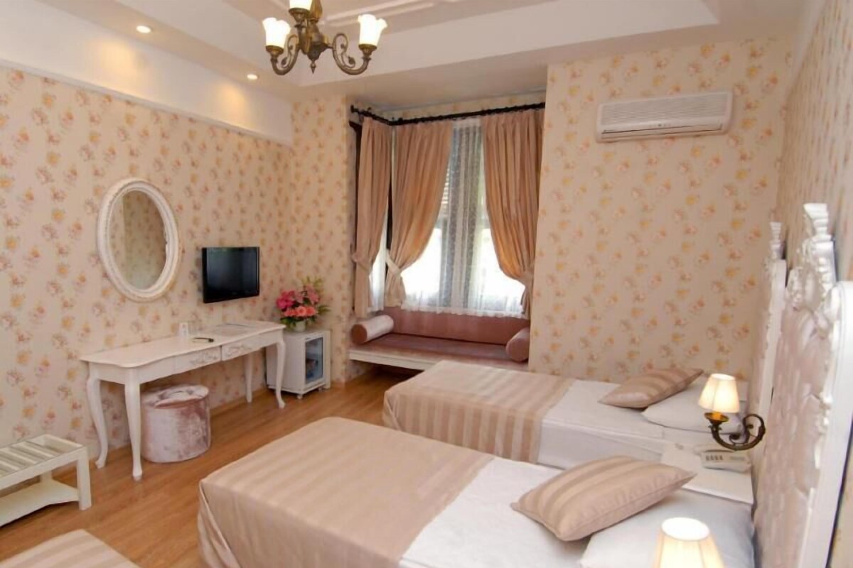Een hotelkamer met twee bedden, een bureau, een televisie, een raam met gordijnen en een airconditioner.