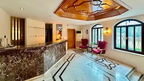 A hotel reception area with a marble counter, red chairs, and a large window with decorative ironwork. - Aspen Hotel - Special Class (Antalya)