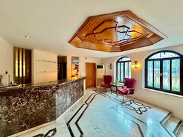A hotel reception area with a marble counter, red chairs, and a large window with decorative ironwork.
