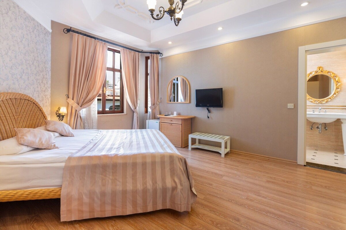 A hotel room with a bed, a television, a small table, and a bathroom with a mirror and sink.