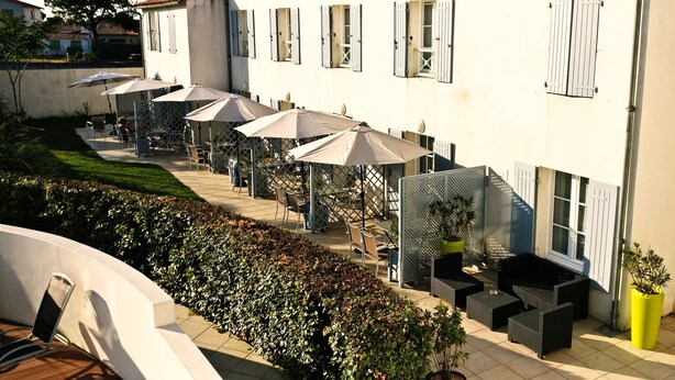A courtyard with outdoor seating, umbrellas, and potted plants. - Appart'hôtel Perle de Ré (La Couarde-sur-Mer)