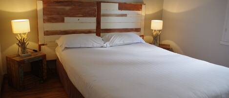 Una cama bien hecha con sábanas blancas en una habitación con cabecera y mesitas de noche de madera.