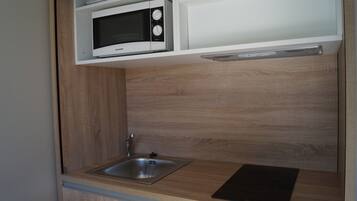Una cocina compacta con microondas, lavamanos y armarios de madera.