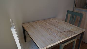 Una mesa de madera pequeña con una silla, un banco blanco y un armario de madera en una habitación de paredes lisas.