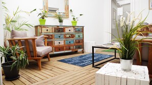 A cozy room with a wooden floor, a wooden chair with cushions, a colorful dresser, and several potted plants. - Appart'hôtel Perle de Ré (La Couarde-sur-Mer)