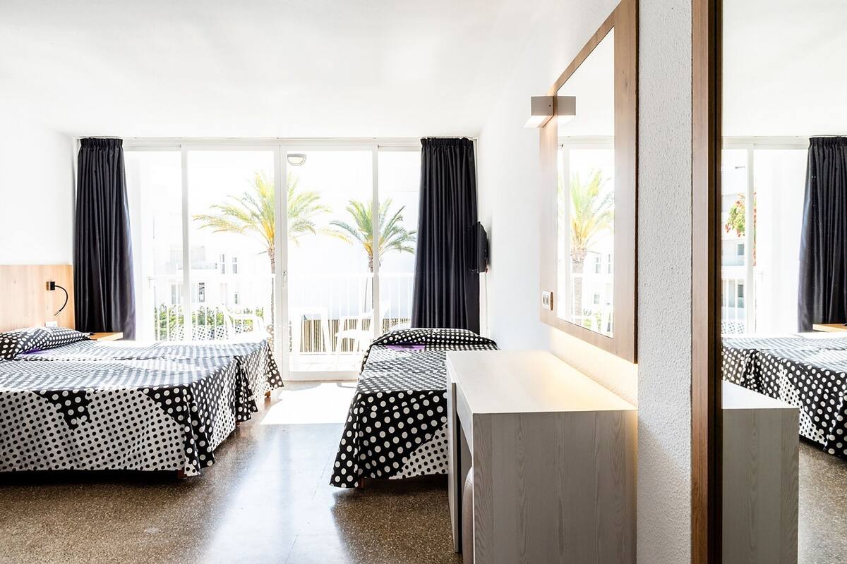 A hotel room with two beds, a large window, and a view of palm trees.