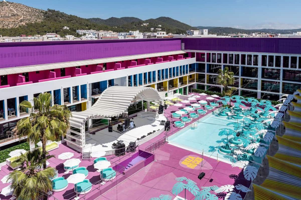 A hotel with a rooftop pool area, multiple balconies, and a view of the surrounding landscape.