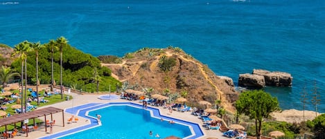 Ein Resort-Pool mit klarem, blauem Wasser, umgeben von Palmen und einer Felsklippe.