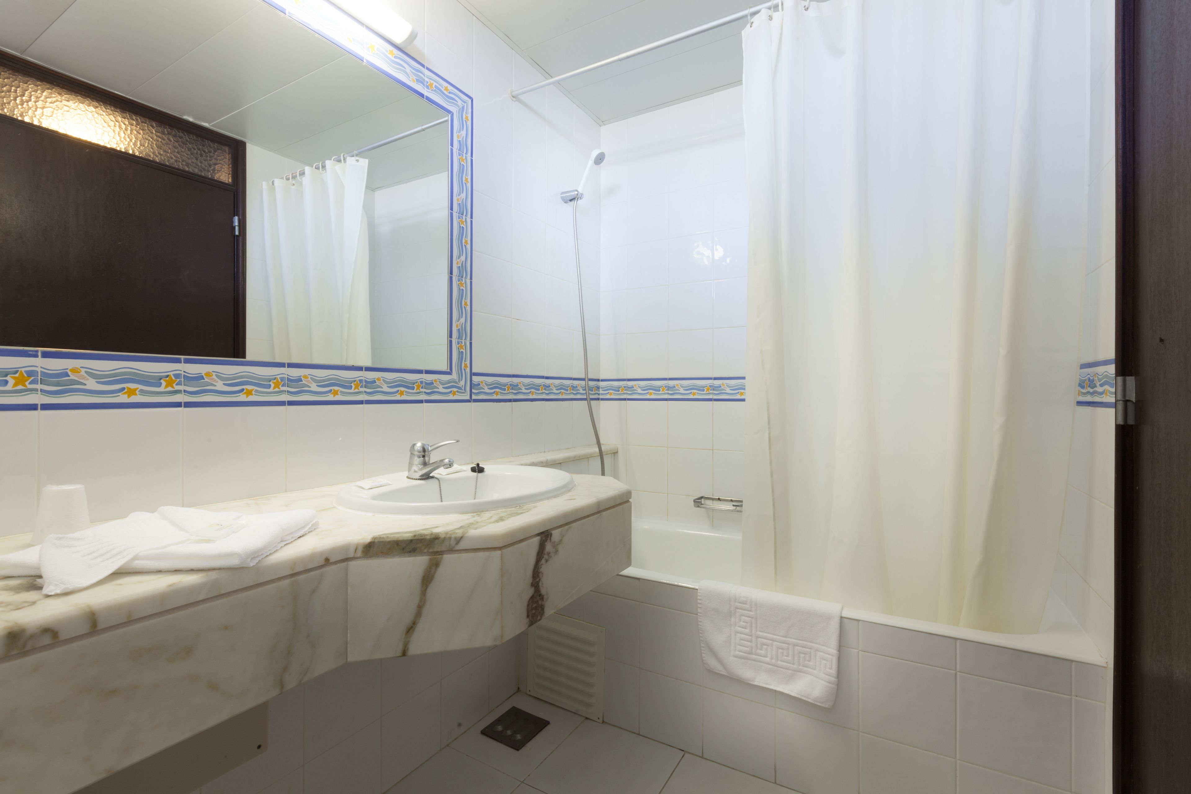 Un baño con lavamanos de mármol, bañera y cortina de ducha.
