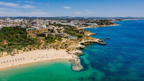 Vista aérea de un pueblo costero con playa de arena, costa rocosa y un gran complejo hotelero con varias edificaciones.