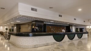 A hotel reception area with a curved counter, seating area, and a large screen. - Hotel Las Palmeras Affiliated by FERGUS (Fuengirola)