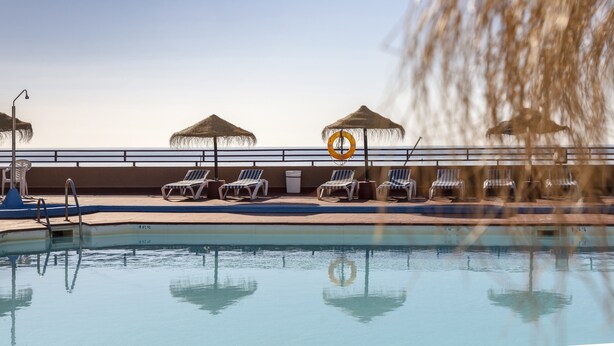 A swimming pool with lounge chairs and umbrellas, a lifeguard chair, and a no swimming sign. - Hotel Las Palmeras Affiliated by FERGUS (Fuengirola)