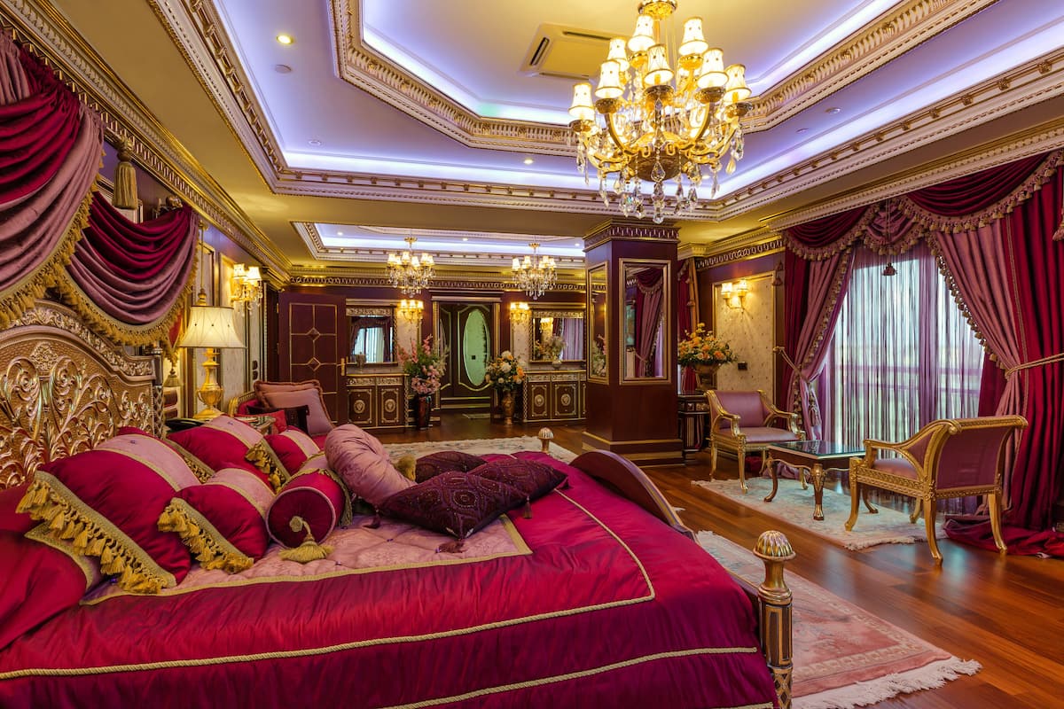 A luxurious bedroom with a large bed, ornate furniture, and a chandelier.